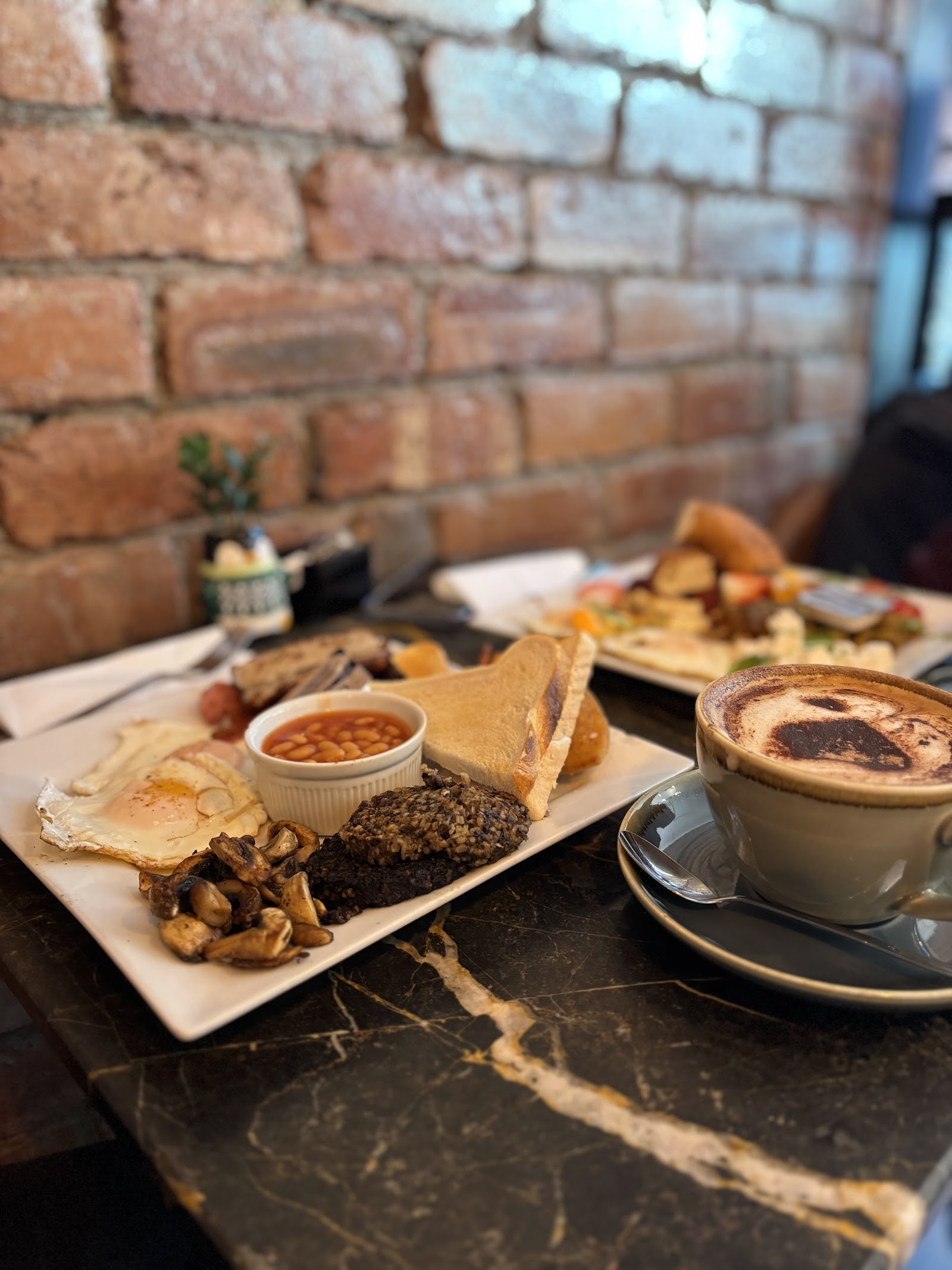 A full Scottish breakfast with black pudding and haggis beside a cappuccino on a marble table