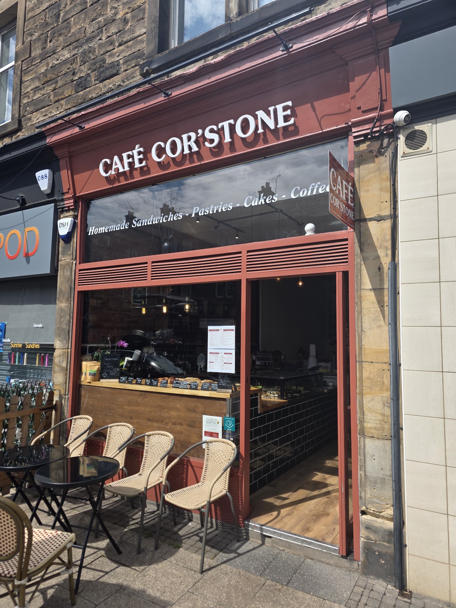 The brick-red Café Cor'stone shopfront with rattan chairs outside